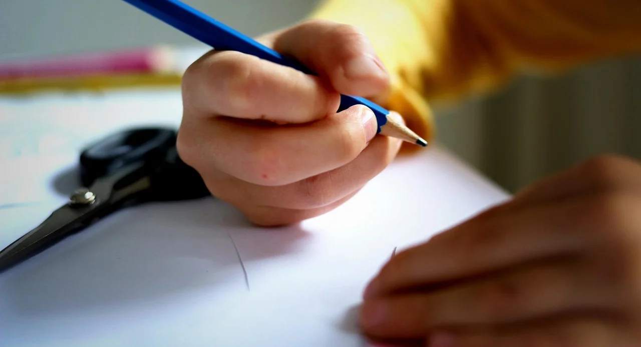Kind schreibt mit Bleistift auf ein Blatt Papier